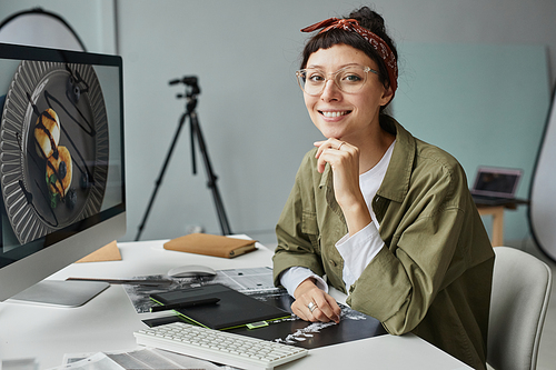 Portrait of young female photographer looking at camera while sitting at workplace in photo studio