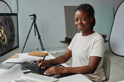 Portrait of black female photographer looking at camera while sitting at workplace in photo studio