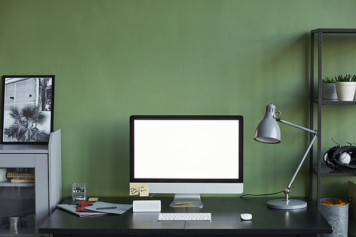 Background image of home office workplace with blank computer screen against green wall, copy space