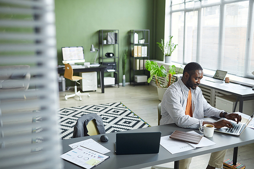 High angle portrait of adult black man working at home office in modern interior and using laptop, copy space