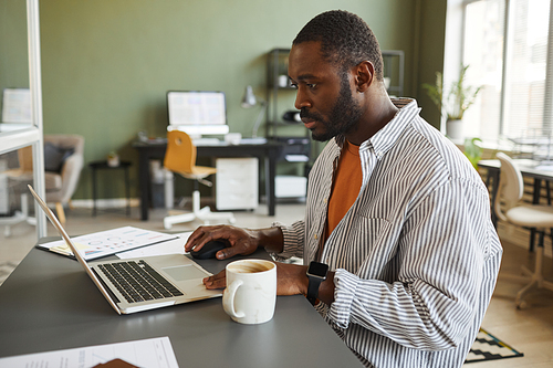 Side view portrait of adult black man working at home office workplace and using laptop, copy space
