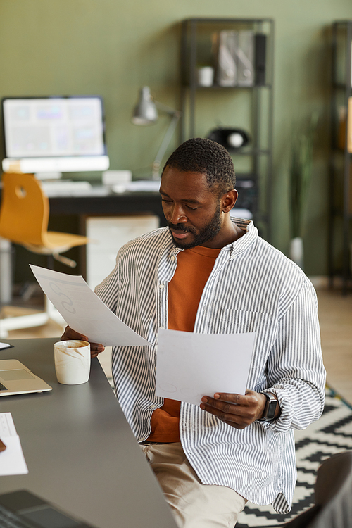 Vertical portrait of modern black businessman working at home office and analyzing documents
