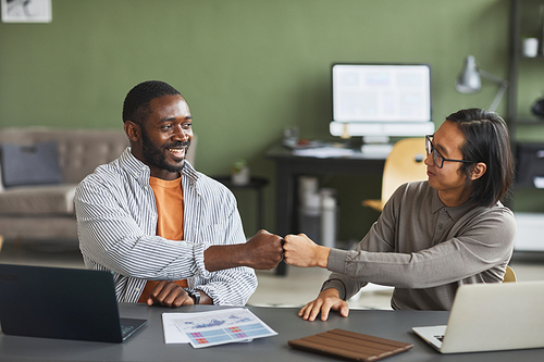 Front view portrait of two ethnic business people African American and Asian fist bumping while working together in office