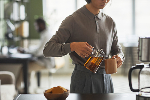 Minimal cropped shot of young Asian man making coffee in office and wearing grey, copy space