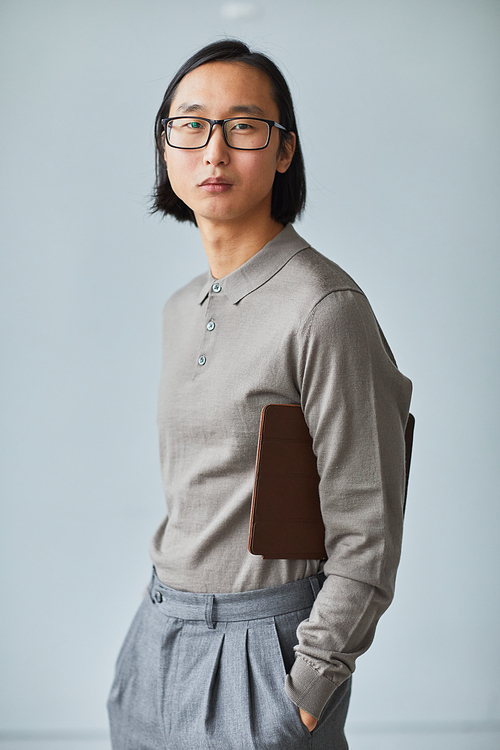 Minimal vertical portrait of young Asian businessman dressed in grey standing against light blue background