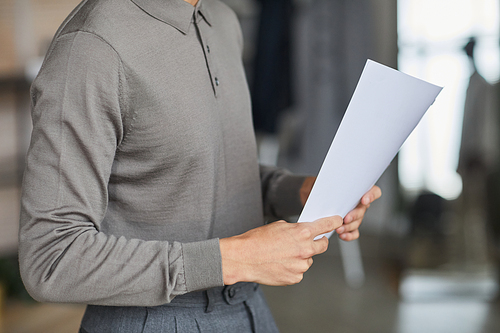 Minimal cropped shot of unrecognizable man holding document and wearing grey in office, copy space