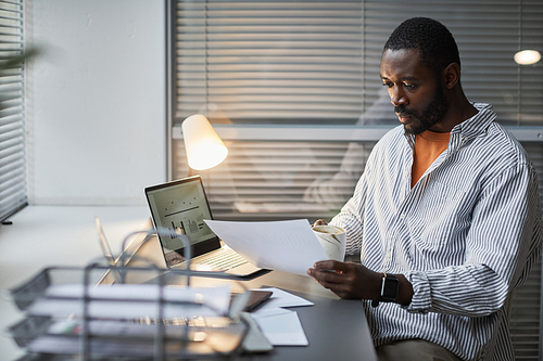 Portrait of adult African American man using laptop while working in white office interior, copy space