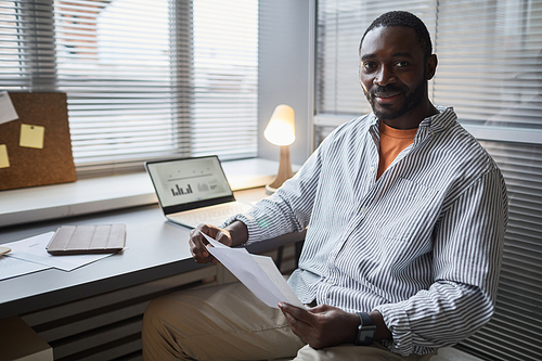 Portrait of smiling black entrepreneur looking at camera while sitting at home office workplace, copy space