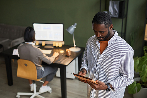Waist up portrait of black businessman using digital tablet while wearing casual clothes in modern office space