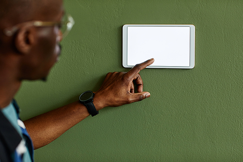 Minimal close up of African American man using smart home control panel with blank screen on green wall, copy space