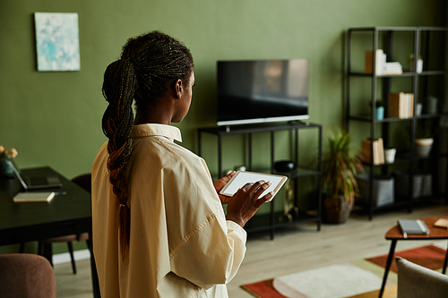 Side view portrait of black young woman holding tablet with blank screen while operating smart home devices, copy space