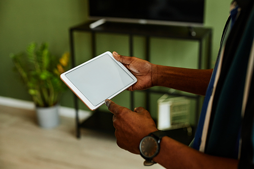 Close up of black young man holding tablet with blank screen while operating smart home devices, copy space