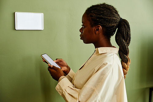 Minimal portrait of young African American woman using smartphone while connecting to smart home system