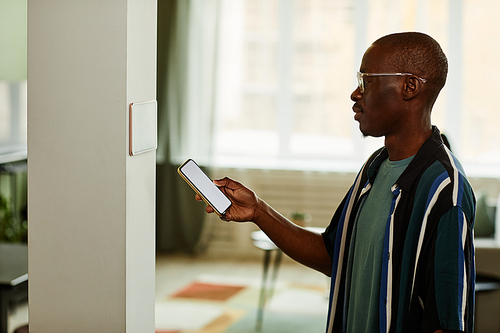 Minimal side view portrait of modern African American man using phone while connecting to smart home system