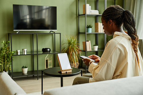 Side view portrait of young black woman connecting phone to smart home system with blank screen, copy space