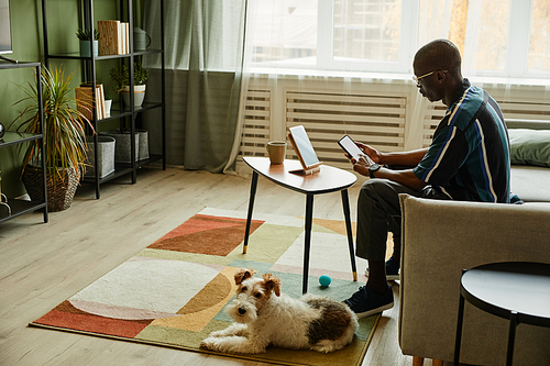 Full length portrait of African American man connecting phone to smart home system in cozy interior, copy space