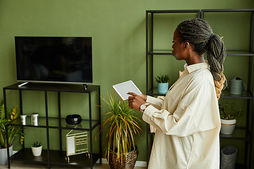 Side view portrait of young black woman operating TV via smart home system with blank screen, copy space