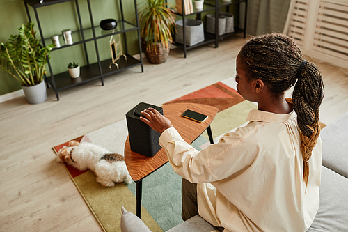 High angle view at young black woman pushing button on smart speaker with home AI, copy space