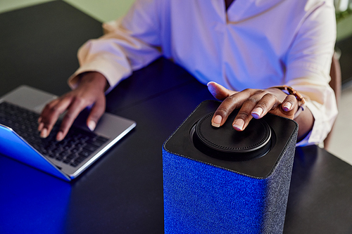 Close up of African American woman operating smart speaker with home AI while working with laptop, copy space
