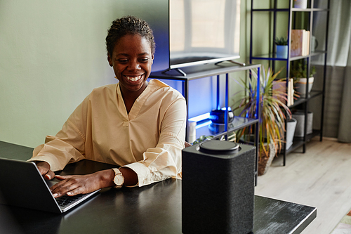 Portrait of smiling African American woman using voice controlled smart speaker while working from home