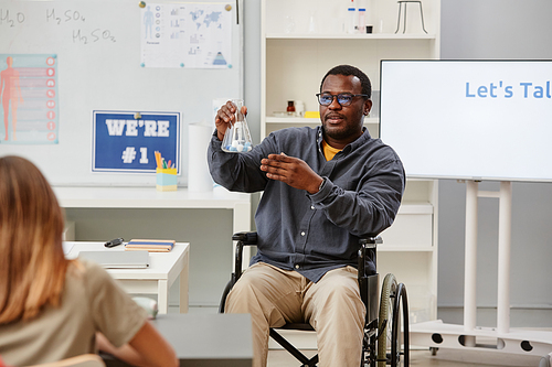 Portrait of African American teacher in wheelchair holding glass beaker during chemistry class in school