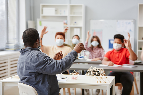 Back view at African American teacher speaking to diverse group of children wearing masks in school classroom , copy space