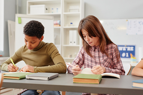 Portrait of two young girls writing in notebooks while studying in school classroom