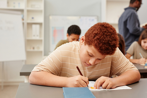 Portrait of red haired teenage boy working hard while studying in school classroom