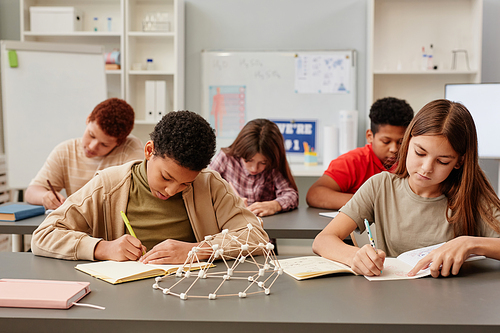 Front view portrait of diverse group of children studying at desks in school classroom with chemistry model in foreground