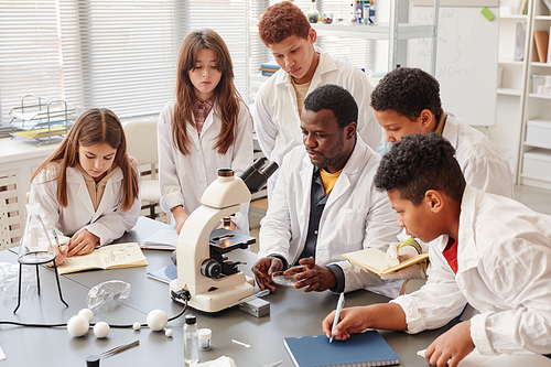 Portrait of diverse group of children doing experiments with teacher in school chemistry lab