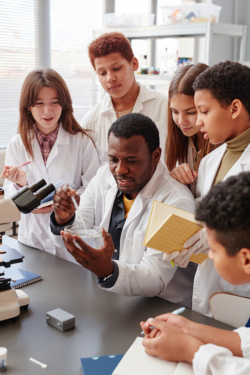 Vertical portrait of diverse group of children doing experiments with teacher in school chemistry lab
