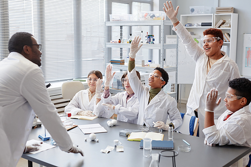 Diverse group of excited children raising hands while answering questions in chemistry class at school