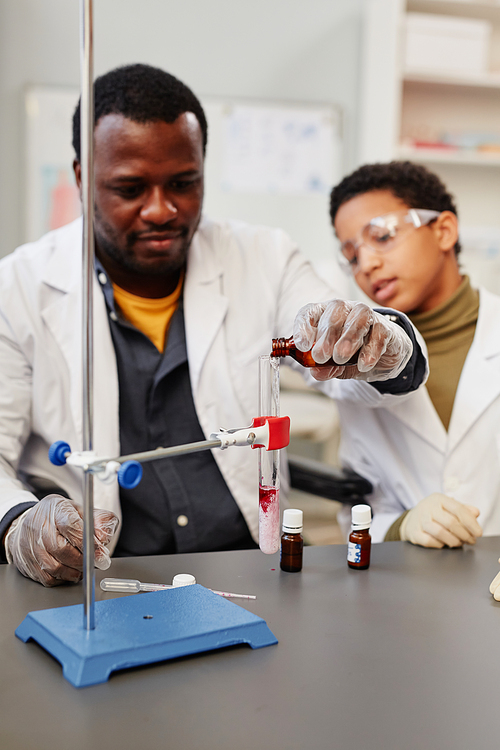 Vertical portrait of African American teacher demonstrating science experiments in school chemistry lab