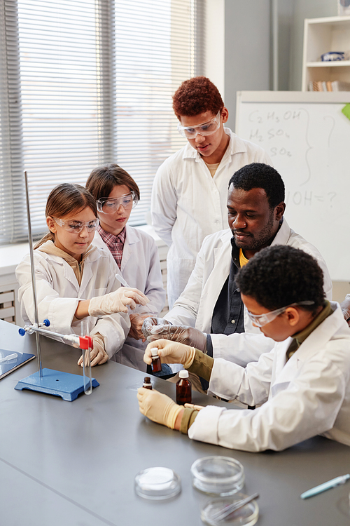 Vertical portrait of African American teacher demonstrating science experiments to group of children in chemistry lab at school