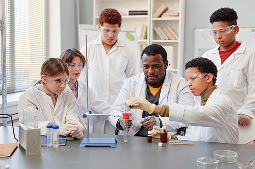 Portrait of African American teacher demonstrating science experiments to diverse group of children in chemistry lab at school