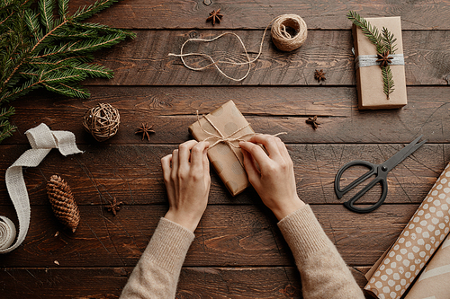 Top view Christmas background with unrecognizable young woman wrapping gifts at wooden table, copy space