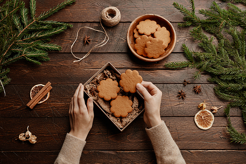 Top view Christmas background with unrecognizable young woman packing homemade cookies in gift wrap at wooden table, copy space