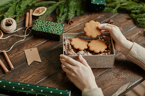 Close up of unrecognizable young woman packing homemade cookies in Christmas gift wrap at rustic wooden table, copy space