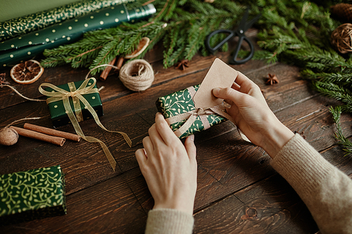 Closeup of unrecognizable young woman wrapping Christmas gifts at rustic wooden table, copy space