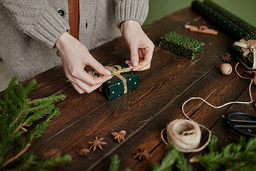 Close up of unrecognizable woman wrapping Christmas present at rustic wooden table, copy space