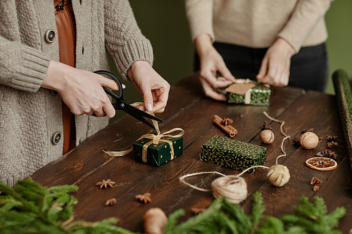 Close up of two unrecognizable women wrapping Christmas presents at rustic wooden table, copy space