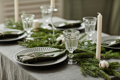 Close up background image of elegant dining room setting for Christmas with table decorated with fir trees and candles, copy space