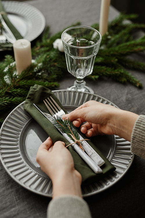 Vertical close up of young woman setting up dining table decorated for Christmas with fir branches and candles