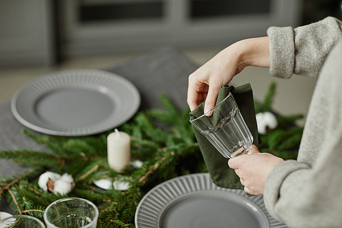 Side view close up of young woman setting up plates on dining table decorated for Christmas with fir branches and candles in grey tones, copy space