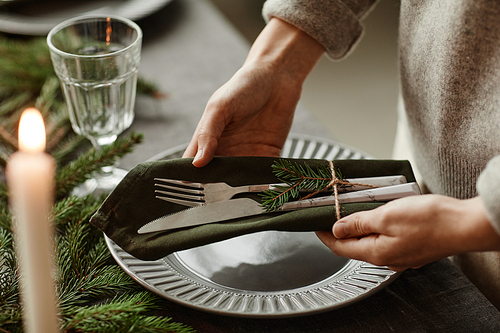 Close up of unrecognizable woman setting up dining table decorated for Christmas with fir branches and candles in grey tones, copy space