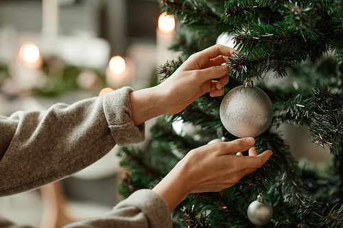 Side view close up of young woman decorating Christmas tree at home in elegant silver and grey tones, copy space