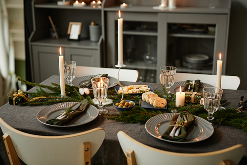 Background image of cozy table setting decorated for Christmas with candles lit in grey tones, copy space