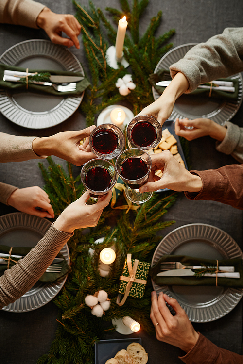 Top view background of four people enjoying Christmas dinner together and toasting with wine glasses while sitting by elegant dining table with candles