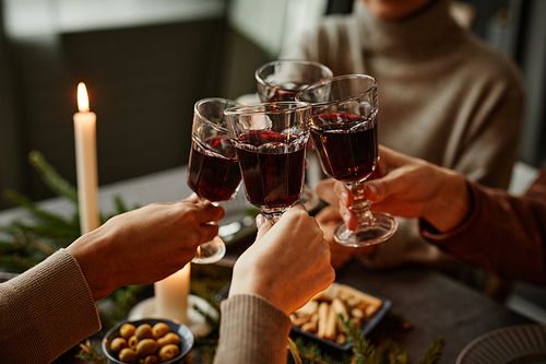 Close up of four people enjoying Christmas dinner together and toasting with wine glasses while sitting by elegant dining table with candles