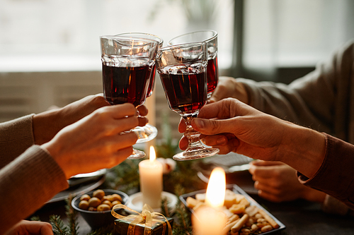 Close up of friends enjoying Christmas dinner together and toasting with wine glasses while sitting by elegant dining table with candles